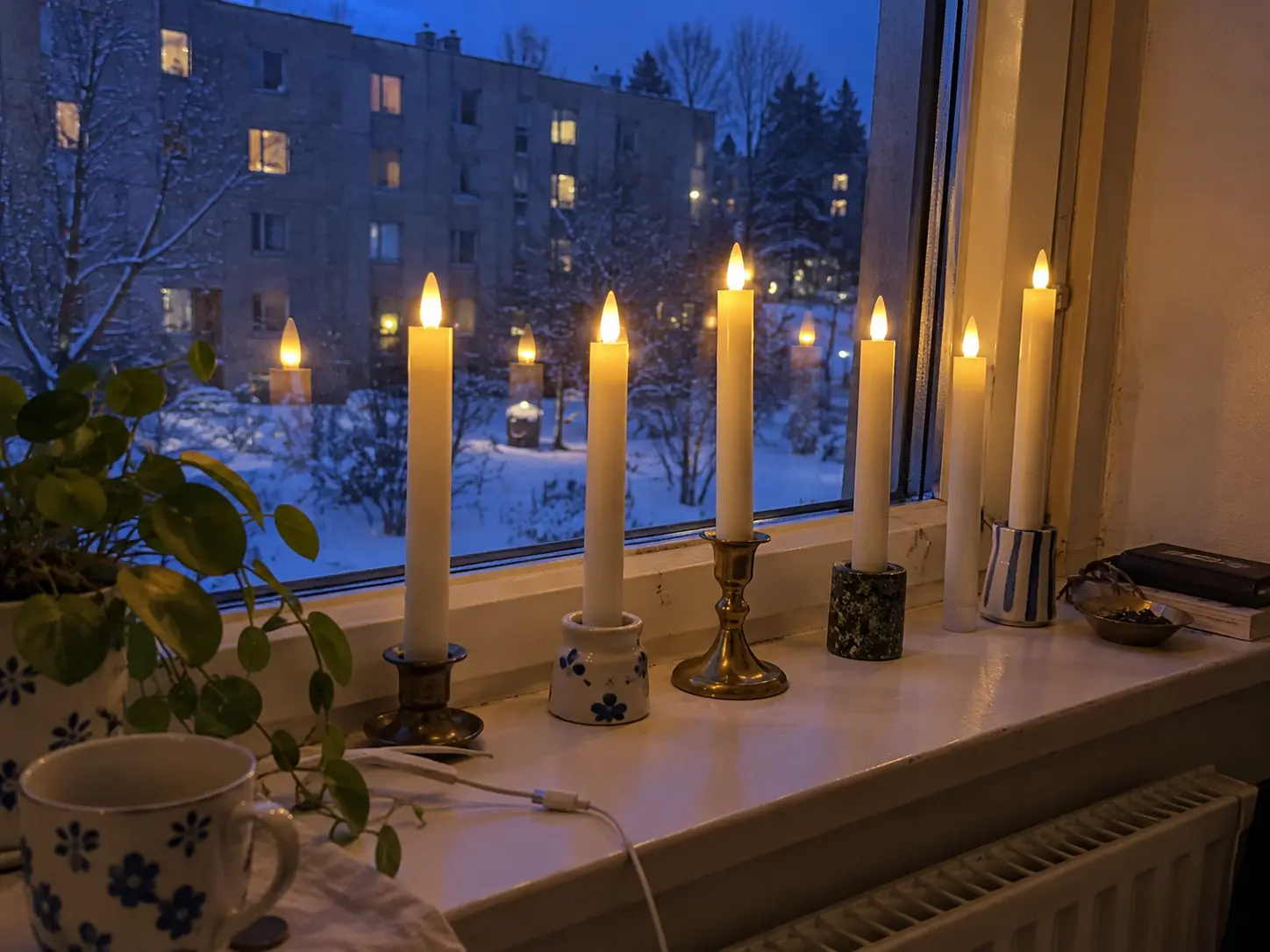 Tända kronljus i ett fönster i ett studentrum en vinterkväll